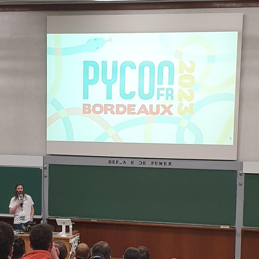 Projection dans un amphithéatre du logo de la conférence francophone sur le langage de programme Python (Pycon Fr 2023 - Bordeaux, avec des serpents multicolores en fond)